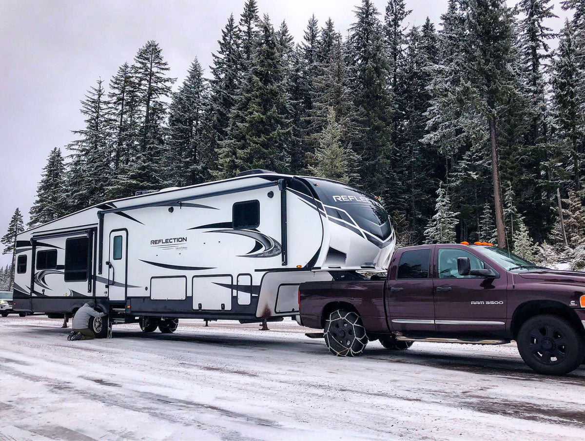 Fifth wheel RV and pickup truck parked at a snowy campsite
