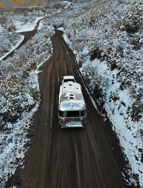 Aerial view of an RV driving a snowy forest road
