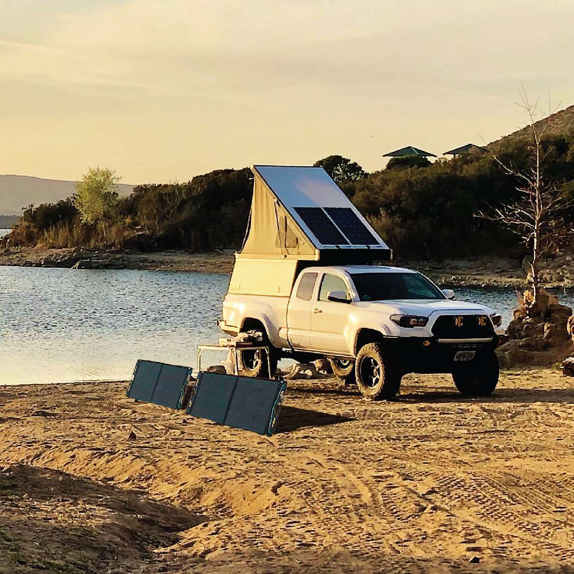 Pickup truck camper with rooftop solar and portable panels at a lake
