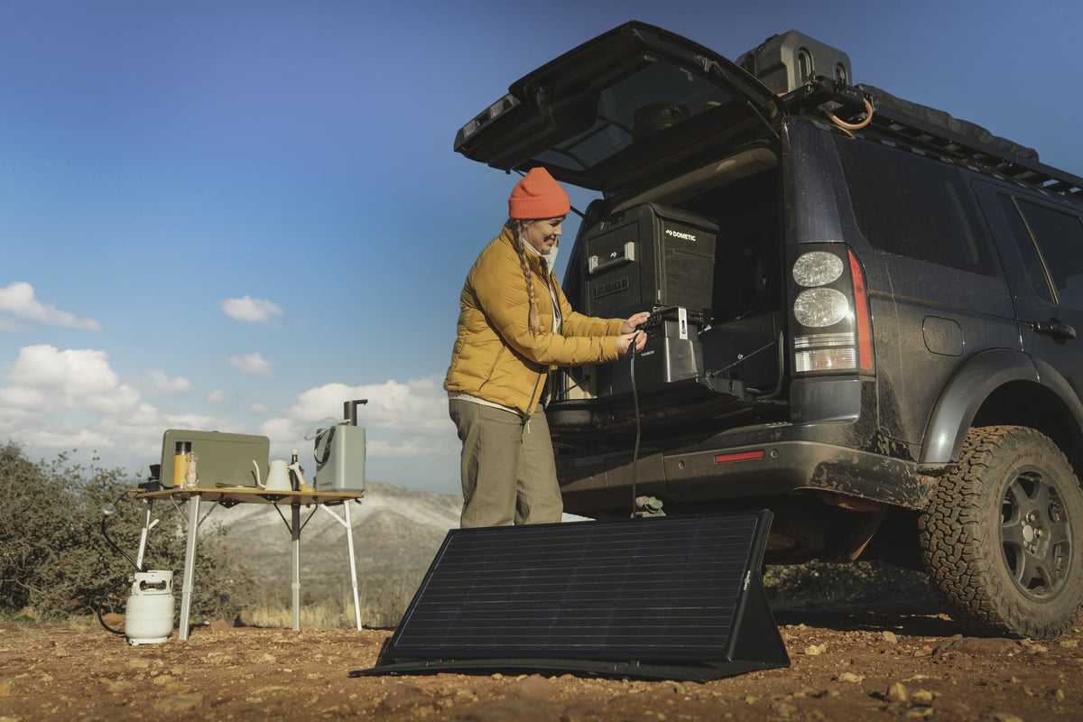 Overlander charging a portable power station from a folding portable solar panel at camp