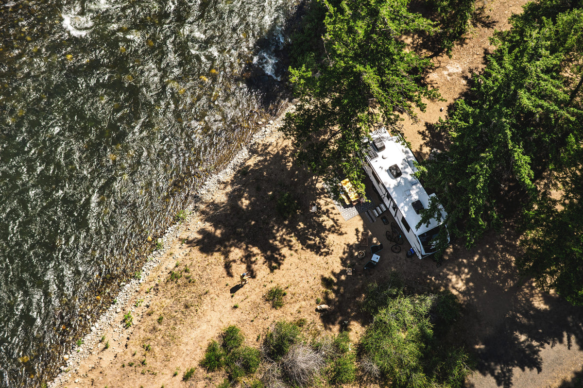 Aerial view of a Jayco travel trailer camped under pine trees beside a river