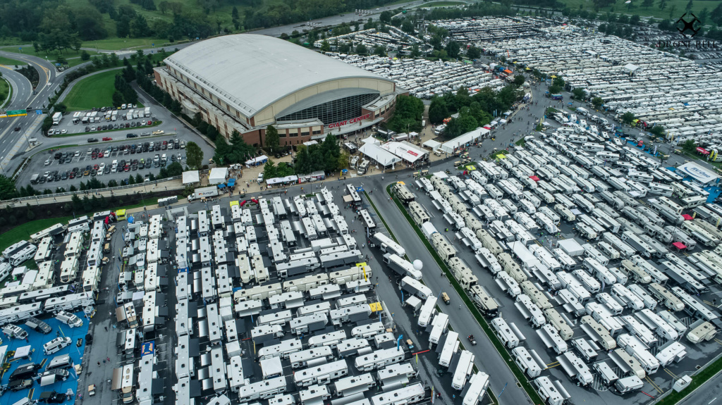 An aerial view of the Hershey RV show, showcasing a sprawling outdoor event with rows of gleaming recreational vehicles (RVs) of various sizes and designs. People can be seen exploring the RVs, and colorful tents and booths line the pathways, creating an exciting atmosphere for RV enthusiasts.